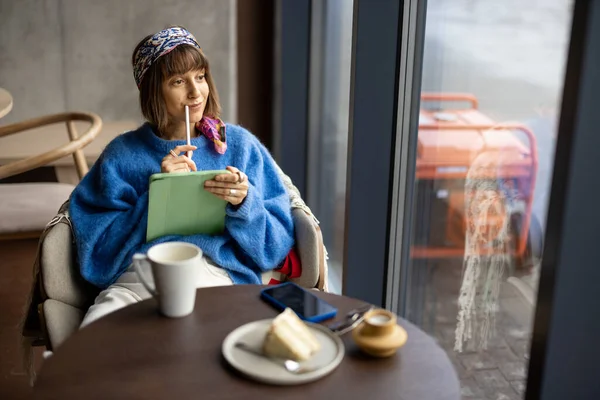 Young stylish woman works on digital tablet while sitting at coffee shop with electric generator outdoors. Concept of working online during blackout