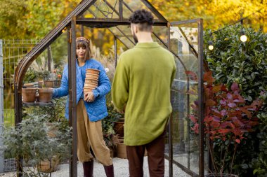 Erkek ve kadın bitkilerle ve çiçeklerle ilgileniyor arka bahçede küçük bir portakalla bahçeyle uğraşıyorlar. Hobi ya da küçük aile işi çiçek yetiştirme konsepti