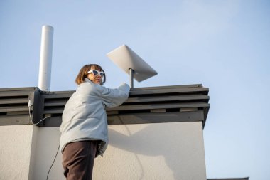 LVIV, UKRAINE - January, 2023: Woman installing Starlink satellite dish on roof of her house. Starlink is a satellite internet constellation operated by SpaceX