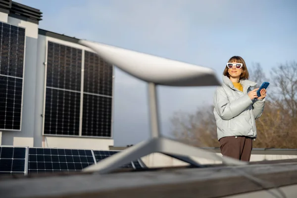 Woman with phone uses satellite Internet on the roof of her house equipped with solar panels. Concept of new technologies and satellite communication