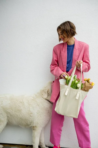 身穿粉红西服 头戴环保手提包 头戴白色背景花朵的时尚女人 旁边有一只白狗 有空隙的帆布袋 — 图库照片