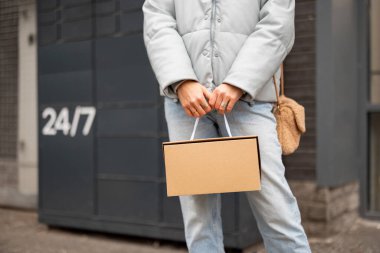 Woman holds a cardboard box on background of automatic post office machine. Concept of modern technologies in self delivery services
