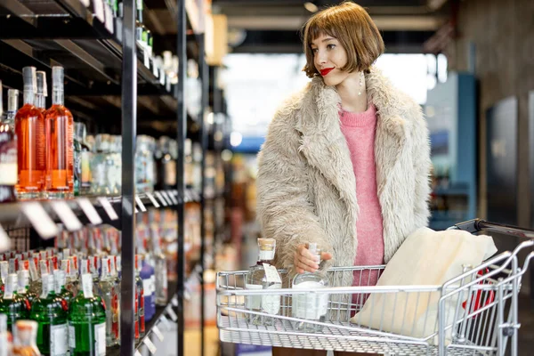 Mulher Escolhe Álcool Forte Estando Com Carrinho Compras Entre Fileiras — Fotografia de Stock