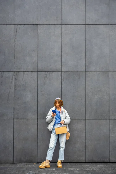 Young Stylish Woman Uses Mobile Phone While Standing Background Gray — Stock Photo, Image