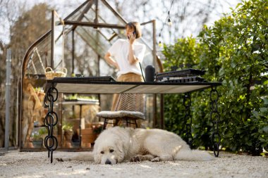 Genç bir kadın bahçede ya da küçük bir dükkanda çiçeklerle ilgilenirken telefonla konuşuyor. Çiçek yetiştirme işi kavramı