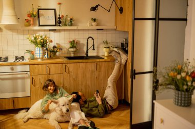 Genç çift mutfaktaki sevimli bir köpekle birlikte rahatça oturuyorlar. Ev konforu ve ev hayatı konsepti