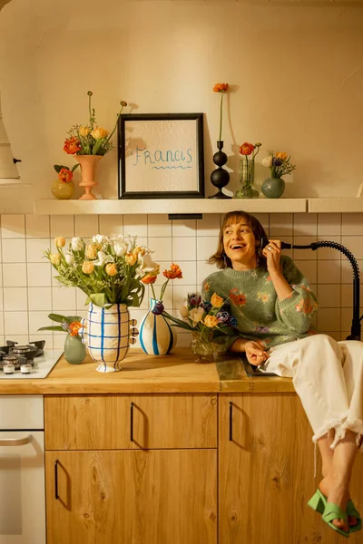 在用鲜花装饰的现代厨房室内装饰的厨房水池上坐着可爱而悠闲的女人 家庭风格 美感和装饰观念 — 图库照片