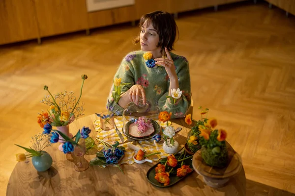 年轻的女人在餐桌边享用着一餐 桌上摆满了花瓶和盘子里的不同花朵 美与花卉饮食的概念 — 图库照片