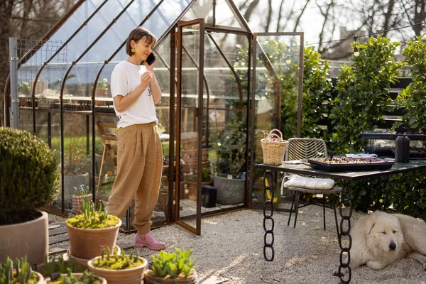 Wanita Muda Berbicara Telepon Sambil Mengurus Tanaman Kebun Atau Toko — Stok Foto