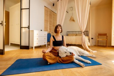 Genç bir kadın sevimli köpeğini önemsiyor, evde yoga yaparken birbirine sarılıyor. Köpek terapisi ve akıl sağlığı kavramı
