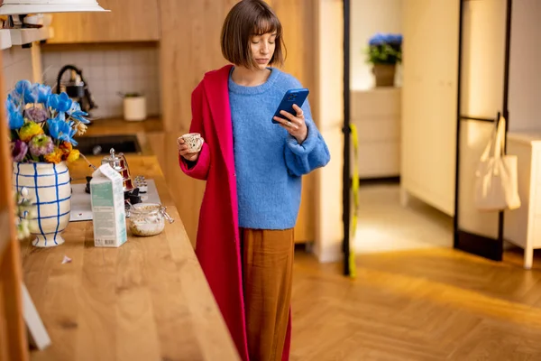 女人冲出家门 穿上外套 喝完咖啡 看了看智能手机 日常工作和繁忙工作的概念 — 图库照片