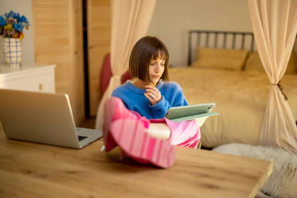穿着五颜六色休闲装的年轻女性在平板电脑和笔记本电脑上工作 而坐在舒适的家庭氛围中 放松地坐在桌旁 家庭办公和远程工作的概念 — 图库照片