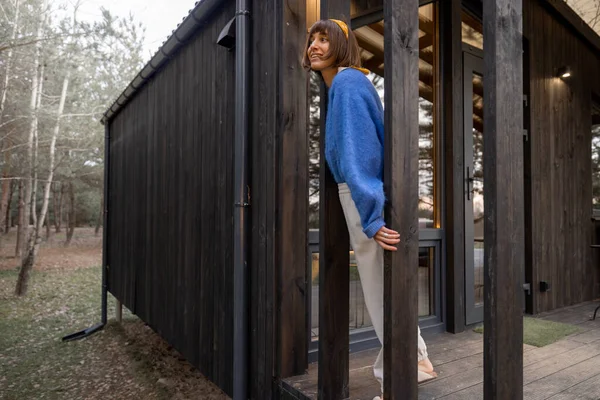 年轻的女人站在松树林的一座木头房子的门廊上 享受大自然 在乡间的小木屋里休息 — 图库照片