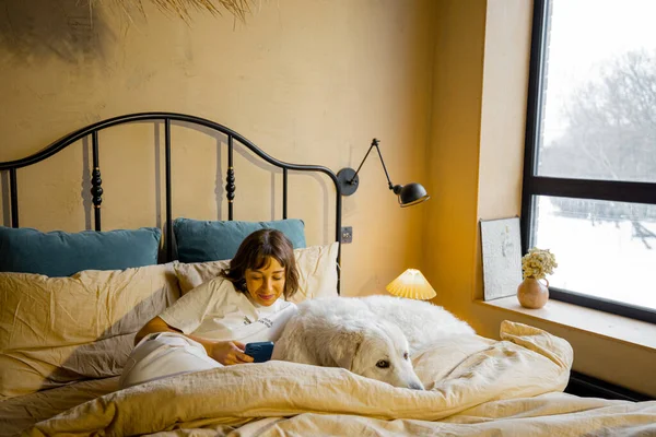 Jonge Vrouw Gebruikt Een Smartphone Terwijl Met Haar Hond Bed — Stockfoto