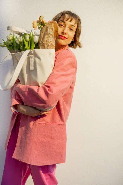 Κομψό Γυναίκα Ροζ Κοστούμι Μεταφέρει Οικολογική Τσάντα Γεμάτη Λουλούδια Λευκό — Φωτογραφία Αρχείου