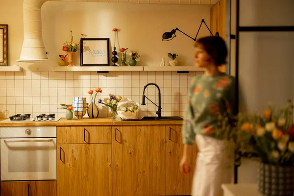 现代厨房的内部用自然材料制成 表面是木制的 架子是开着的 装饰着鲜花 动作模糊了前面的女性形象 — 图库照片