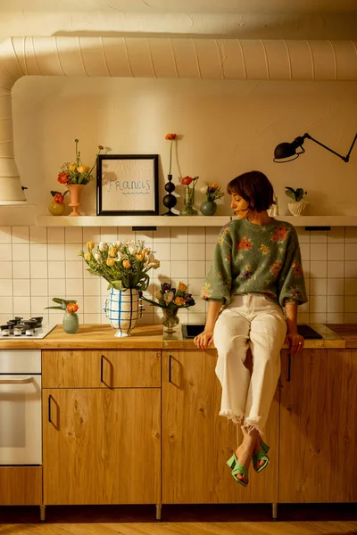 漂亮的女人坐在用鲜花装饰的现代化厨房的厨房桌子上 家庭风格和装修概念 — 图库照片