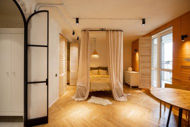 Doğal malzemelerle yapılmış bej tonlarda şık stüdyo dairenin iç görünüşü. Kanopili yatak odası.