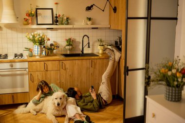 Genç çift mutfaktaki sevimli bir köpekle birlikte rahatça oturuyorlar. Ev konforu ve ev hayatı konsepti