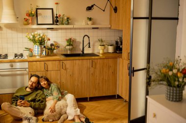 Genç çift mutfaktaki sevimli bir köpekle birlikte rahatça oturuyorlar. Ev konforu ve ev hayatı konsepti