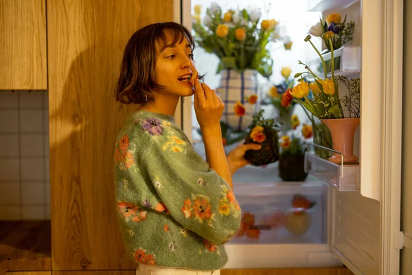 可爱的女人打开装满鲜花的冰箱 站在厨房里 食用花的概念与美花的饮食 — 图库照片