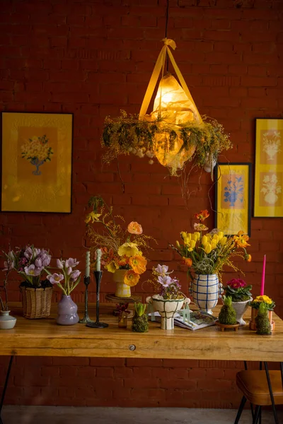 Beautiful dining table decorated with flowers in living room with brick wall and pictures behind