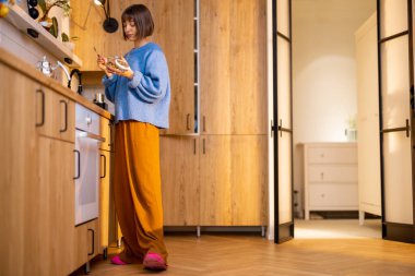 Genç bir kadın modern stüdyo dairesinin mutfağında kahvaltı hazırlıyor. Yurtiçi yaşam tarzı ve iç konsept