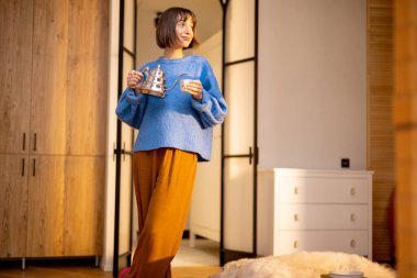 Genç bir kadın modern stüdyo dairesinin mutfağında çaydanlık ve fincanla boş zamanlarını geçirir. Yurtiçi yaşam tarzı ve sağlık konsepti