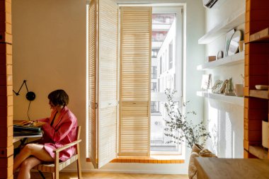 Pembe elbiseli kadın, modern ve şık bir apartmanın çalışma odasında otururken biraz kitap okuyor.