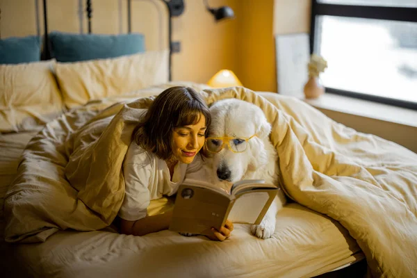 Молодая Женщина Своей Милой Собакой Очках Читает Книгу Лежа Вместе — стоковое фото