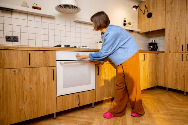 女人控制烤箱 在家里用现代厨房用具做饭 现代和新厨房设备的概念 — 图库照片