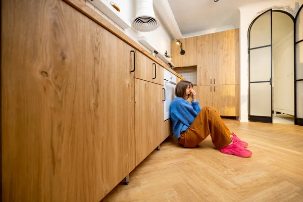 寂寞的女人坐在一间现代化的室内厨房的地板上 视野开阔 有复制的空间 沮丧和孤独的概念 — 图库照片