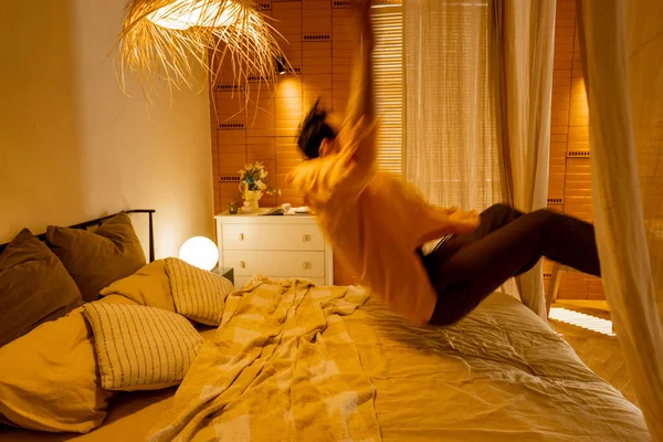 男人在舒适的米黄色卧室里跳上床 人在运动中模糊不清 家居舒适和放松的概念 — 图库照片
