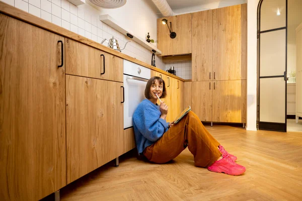 年轻女子坐在新的时尚工作室公寓的厨房地板上 带着一个数码平板电脑 在家远程工作或闲暇时间的概念 — 图库照片
