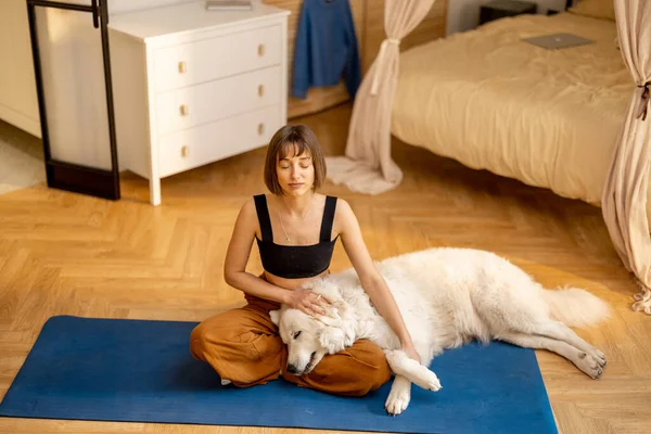 Genç bir kadın sevimli köpeğini önemsiyor, evde yoga yaparken birbirine sarılıyor. Köpek terapisi ve akıl sağlığı kavramı