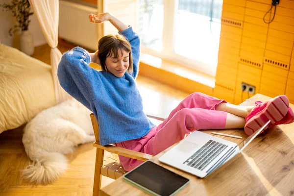 自宅のノートパソコンで作業中にテーブルのそばに座りながらリラックスする女性 居心地の良いホームオフィスで快適に感じています 余暇とリモートワークの概念 — ストック写真