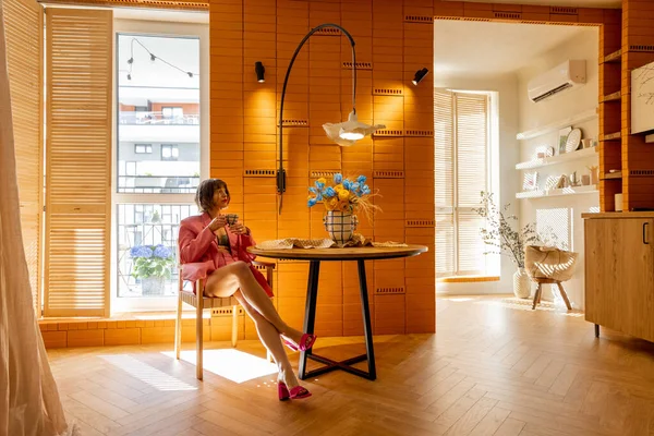 身着粉红西服的女人坐在时尚舒适的公寓工作室里的餐桌旁 感到很放松 — 图库照片