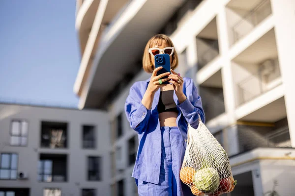 Молодая Женщина Пользуется Телефоном Идет Домой Сеткой Полной Свежих Продуктов — стоковое фото