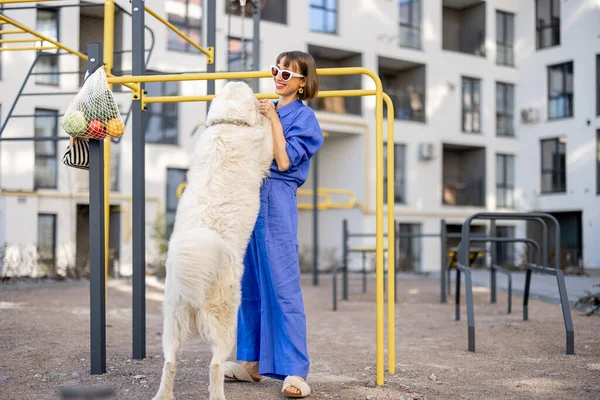 女人和她的大白狗在公寓楼的运动场上玩耍 一起玩乐 一起在户外消磨时光 — 图库照片