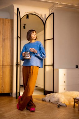 Genç bir kadın modern stüdyo dairesinin mutfağında çaydanlık ve fincanla boş zamanlarını geçirir. Yurtiçi yaşam tarzı ve sağlık konsepti