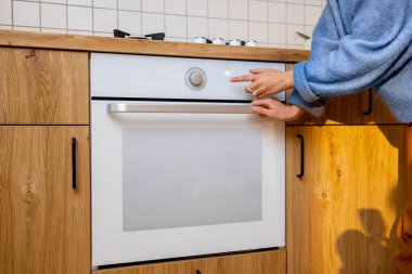 Kadın fırını kontrol ediyor, evde modern mutfak aletlerini kullanarak yemek pişiriyor, yakın çekim manzarası var. Modern ve yeni mutfak ekipmanları kavramı