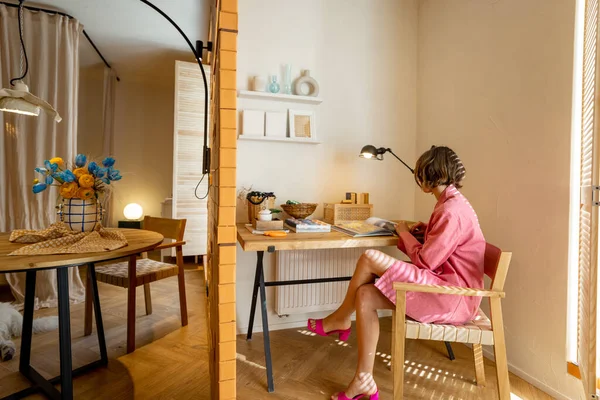 穿着粉色西服的女人坐在时尚时尚的现代公寓工作室的工作区边看书 — 图库照片