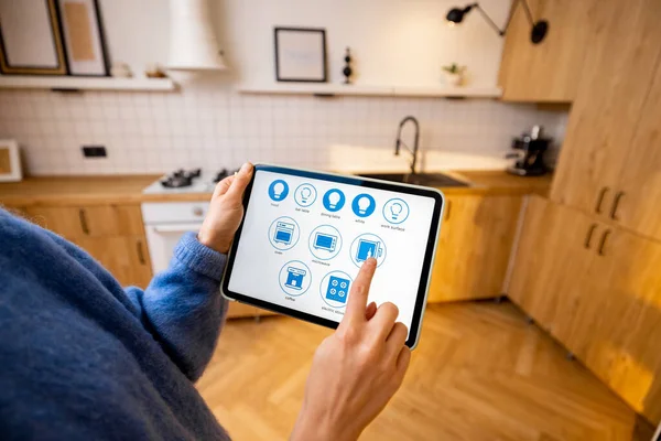 Woman holds a digital tablet with running smart home program, controlling smart kitchen appliances. Close-up on screen. Concept of new technologies for comfort living