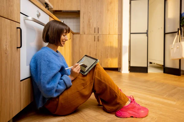 Bir Kadın Mutfak Zemininde Otururken Dijital Tablet Üzerinde Mutfak Tasarımı — Stok fotoğraf