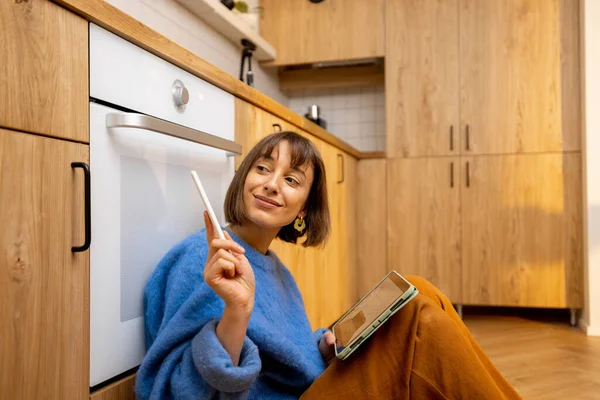 Woman designing kitchen interior on a digital tablet while sitting on a kitchen floor at new apartment. Concept of easy interior design using digital devices