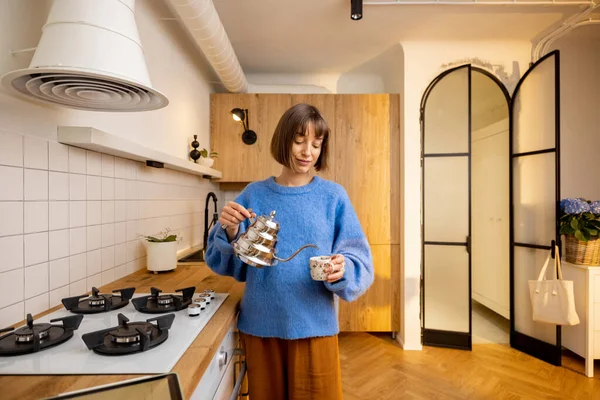 年轻的女人在现代厨房的内部用水壶和杯子煮咖啡 家庭生活方式的概念 — 图库照片