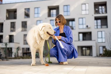 Kadın köpeğinin pisliğini temizliyor, plastik torbaya kakasını koyuyor, apartmanın iç bahçesinde yürürken...