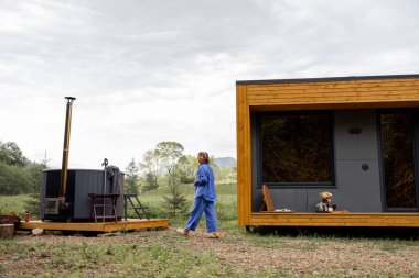 Yakınlarda jakuzisi olan bir kadın, ahşap evde doğanın üzerinde dinleniyor. Eğlence ve doğaya kaçış kavramı.