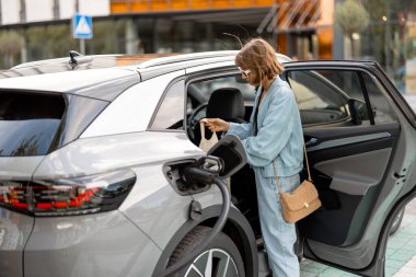 Kadın, satın alınmış ürünleri süpermarketten şarj istasyonuna kadar elektrikli arabasının arka koltuğuna koyar.