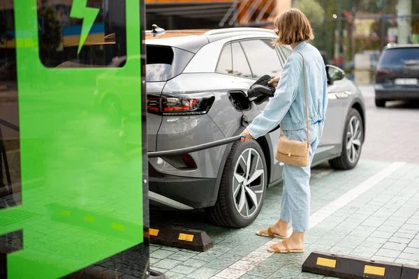 年轻女子在室外的公共收费站插上电缆 以便快速充电 电动汽车收费 电力和绿色能源的概念 — 图库照片